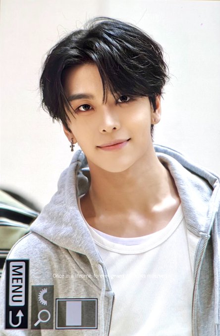 A young man with dark, tousled hair and a subtle smile poses in a gray hoodie over a white shirt, wearing a small hoop earring. The image appears to be a screenshot from a video menu, with "MENU" and playback icons visible at the bottom, highlighting his striking facial features—fitting the caption's emphasis on "Face is crazy!!" referring to Xinlong from Alpha Drive One.