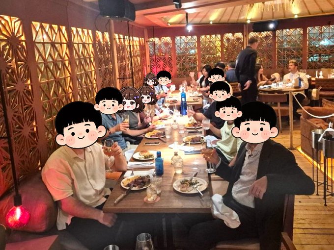 A group of people having dinner at a long table in a restaurant, with their faces obscured by cartoon face stickers.