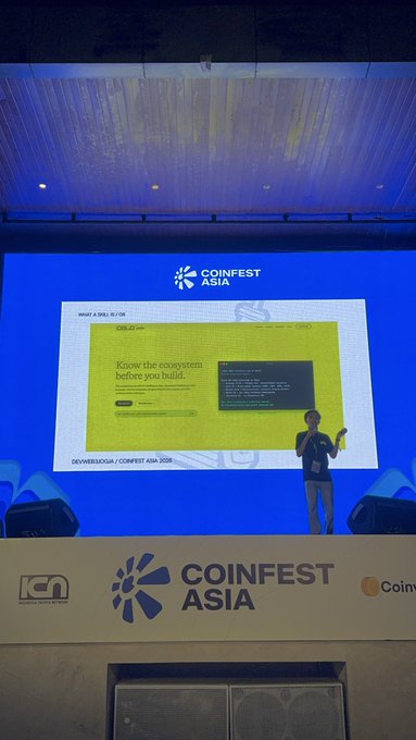 A presenter stands on stage at the COINFEST ASIA conference, presenting a slide titled 'DEVVERSE.IO / COINFEST ASIA 2024' discussing ecosystems and ecosystem building.