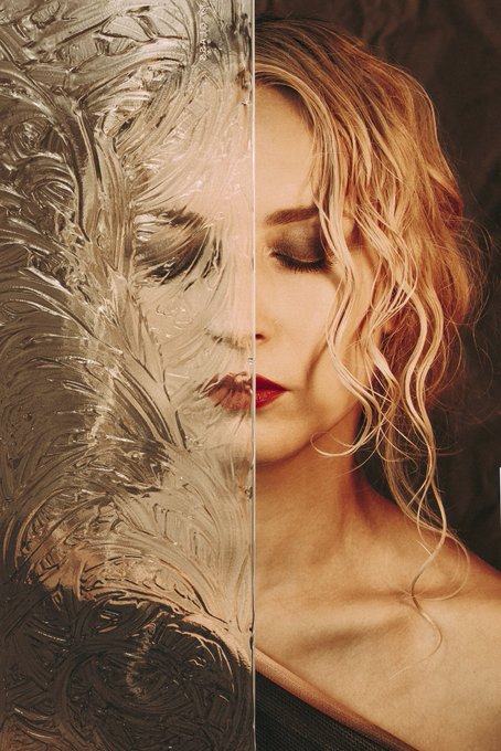 A portrait of a woman with wavy blonde hair, where the left half of her face is obscured by a textured, frosted glass-like overlay.