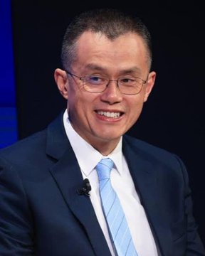 A portrait of an Asian man with short dark hair and glasses, wearing a navy blue suit with a light blue striped tie and white shirt, smiling at the camera against a dark blue background.