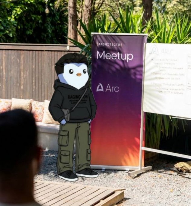 An outdoor event setup featuring a life-sized penguin character cutout wearing a hoodie and cargo pants, standing next to a banner reading '[ARCHITECTS] Meetup Arc' beside a whiteboard.