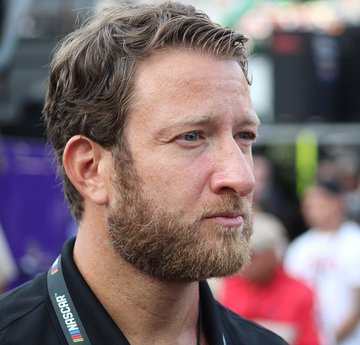 Dave Portnoy, founder of Barstool Sports, is shown wearing an interview lanyard, looking off-camera with a serious expression at what appears to be a public event or sports venue. The image accompanies news of his recent comments about losing millions on Bitcoin while planning to hold his position.