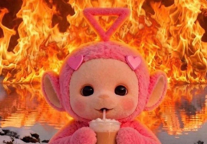A pink plush character with heart ears and a triangular halo sitting in front of a wall of flames while drinking from a cup with a straw.