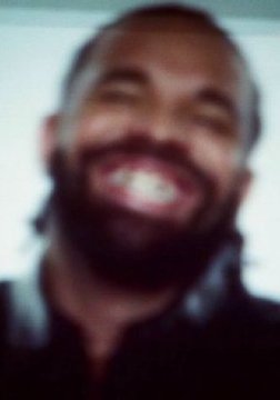 A low-resolution, heavily compressed image of a smiling bearded man.
