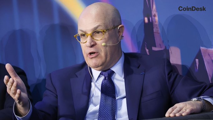 Former CFTC Chair Christopher Giancarlo speaks at a CoinDesk event, gesturing while wearing a dark suit, blue tie, and yellow-framed glasses with a headset microphone. The "CoinDesk" watermark is visible in the upper right corner, linking the image to his commentary on crypto regulation moving forward despite the Senate's failure to pass the CLARITY Act.