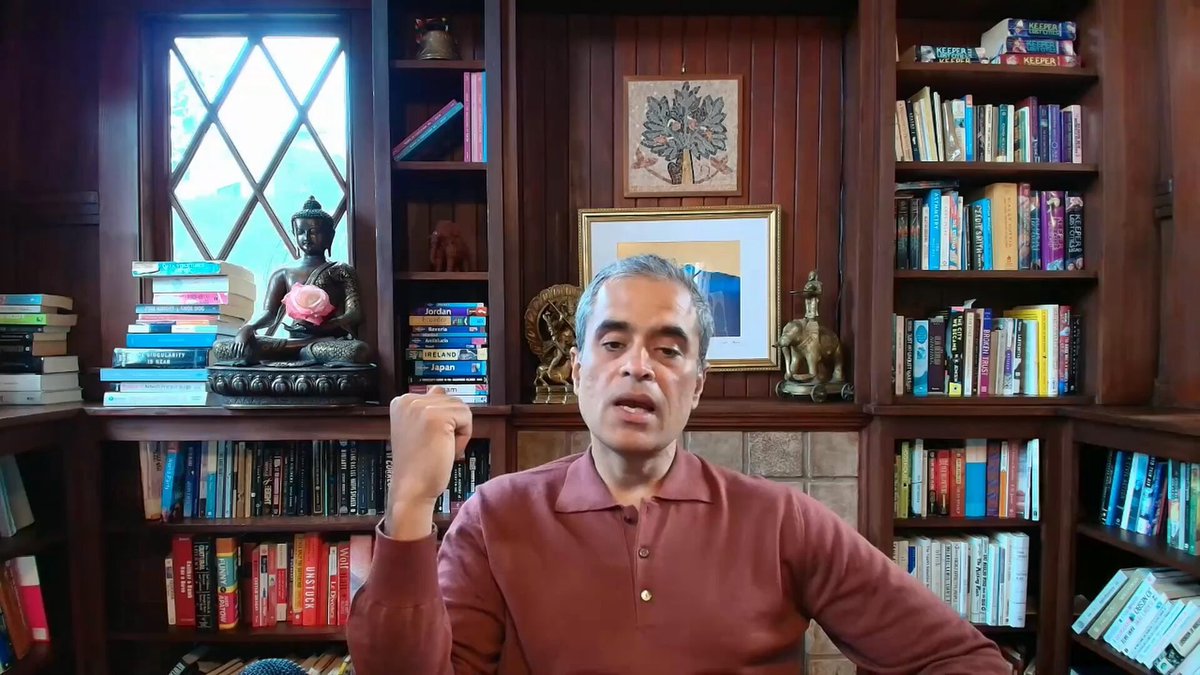 The image shows a man sitting at a desk surrounded by numerous books. The man appears to be wearing a brown shirt and is seated in front of a large window that offers a view of trees outside. There are also several bookshelves filled with various books, indicating an environment conducive to learning or studying. The presence of the man and his surroundings suggests that he might be engaged in some form of intellectual pursuit or work related to finance, as there is a connection between the man's attire and the post about payment systems.