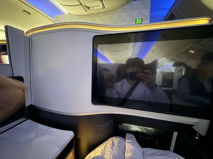 A reflection in an airplane's entertainment screen shows the passenger taking a selfie mid-flight at 40,000 feet, perfectly capturing the "high altitude" contemplation of life and trading that the post references. The blue ambient cabin lighting and luxury business-class setting underscore the aspirational, dream-chasing tone of the caption.