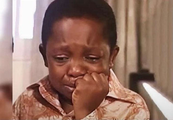 A close-up of a young Black child with a tearful, distressed expression, holding their hand to their mouth.
