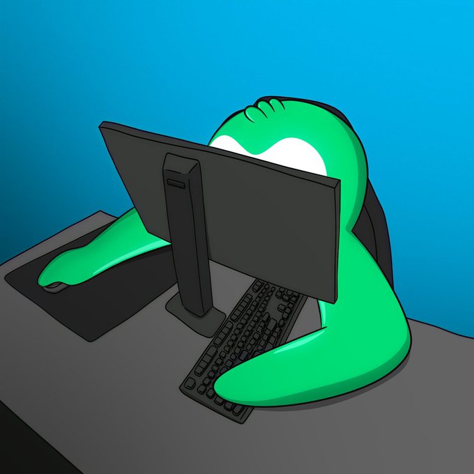 A green cartoon character wearing a mask sits at a computer desk, facing away from the viewer towards a black monitor.