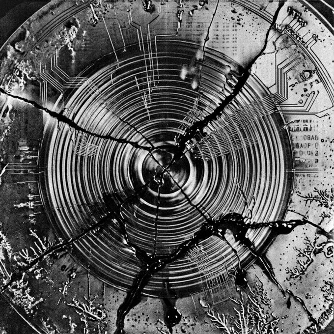 A black and white abstract image depicting a circular, spiraling pattern reminiscent of a vinyl record or radar, overlaid with cracked textures and circuit-like elements.