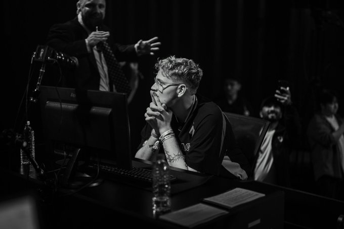 A focused player in glasses intently watches a computer screen during what appears to be a high-stakes gaming or trading event, while another man in a suit gestures animatedly behind him amid an enthusiastic crowd.

The intense concentration and emotional crowd reactions captured in the image align with the dramatic moments referenced in the post—likely showcasing one of the mentioned players experiencing pivotal events like Ethan’s liquidation or Saewoo’s victory, highlighting the live, high-pressure atmosphere of the event.