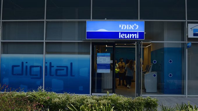 The exterior of a Bank Leumi (לאומי) branch featuring a blue "digital" banner on the window, with people visible entering through the glass doors.