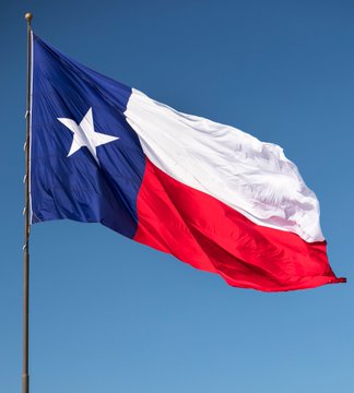 The image features a Texas state flag flying high against a clear blue sky, with the word "Texas" prominently displayed on the flag. The flag appears to be waving in the wind, indicating that it's currently blowing. In the background of the image, there is text that reads "TEXAS IS MOVING FROM BITCOIN ETF EXPOSURE TO DIRECT #BITCOIN CUSTODY THEY ARE USING THE ISHARES BITCOIN ETF AS AN INTERIM MEASURE BEFORE TRANSITIONING TO DIRECT BITCOIN CUSTODY". This suggests that the Texas state flag is being used as a symbol for Bitcoin adoption, and it's likely that the image was taken during or shortly after the transition from BitCoin ETF exposure to direct BitCoin Custody.