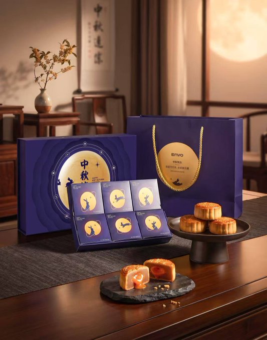 A Mid-Autumn Festival mooncake gift set branded "ENVO" is displayed in elegant dark blue packaging, featuring a box and matching shopping bag set against a softly lit interior with a glowing moon visible through the window, while individually wrapped mooncakes, a golden mooncake cut open to reveal its yolk filling, and decorative calligraphy reading "中秋" (Mid-Autumn) sit on a wooden table, with the accompanying tweet's playful reference to "蛋黄莲蓉" (egg yolk lotus seed paste) linking the image's traditional mooncake imagery to Envo's introduction as a Web3 social platform integrating wallet functionality into social interactions.