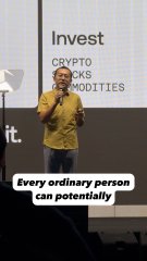 A man in a yellow hoodie speaks in front of a screen listing 'CRYPTO', 'STOCKS', and 'COMMODITIES', with overlaid text reading 'Every ordinary person can potentially'.