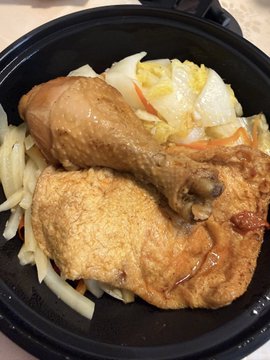 A black bowl filled with Asian-style food including a braised chicken leg/drumstick over rice with cabbage and vegetables in a savory brown sauce.