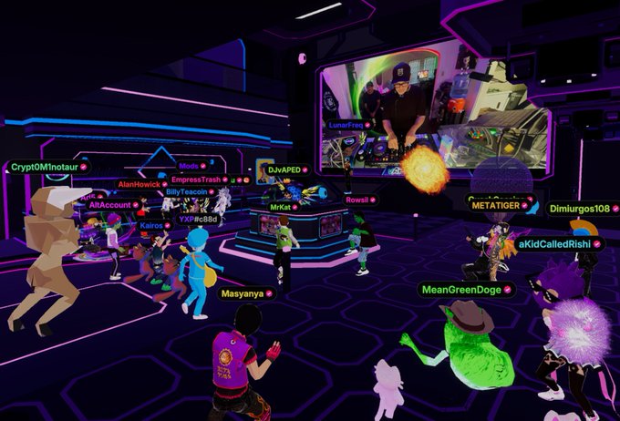 A screenshot from a virtual world/metaverse event showing multiple avatars gathered in a neon-lit room watching a presentation on a large screen.