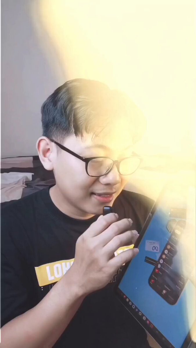 The image features a young man wearing glasses, holding a computer mouse and looking at his phone screen with an expression of surprise or interest. The surrounding environment includes a bed and a chair, suggesting that he might be sitting in a bedroom or a similar setting. The caption for this image reads "This guy is good. Him and @NikolaosDarmls are worth a follow if you want to keep up to date via video shorts on @CronosApp."