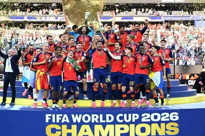 A team in red Spain jerseys celebrating with the FIFA World Cup trophy, with text reading 'FIFA WORLD CUP 2026 CHAMPIONS' at the bottom.