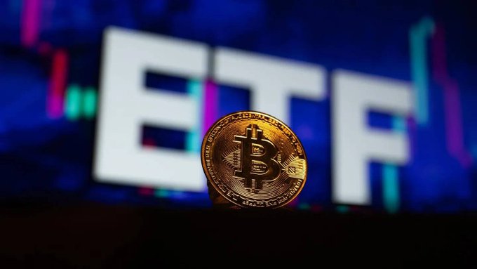 A physical Bitcoin token standing upright in front of a blurred digital display showing the letters "ETF" with colorful trading chart lines in the background.