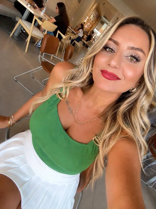 A woman with long blonde hair takes a selfie wearing a green halter top and white skirt, paired with red lipstick and gold jewelry, in what appears to be a bright café setting. The caption "Yeşil iyi geldi sanki" (Turkish for "Green felt good, I guess") playfully matches her vibrant green outfit, suggesting a mood-boosting effect from wearing the cheerful color.