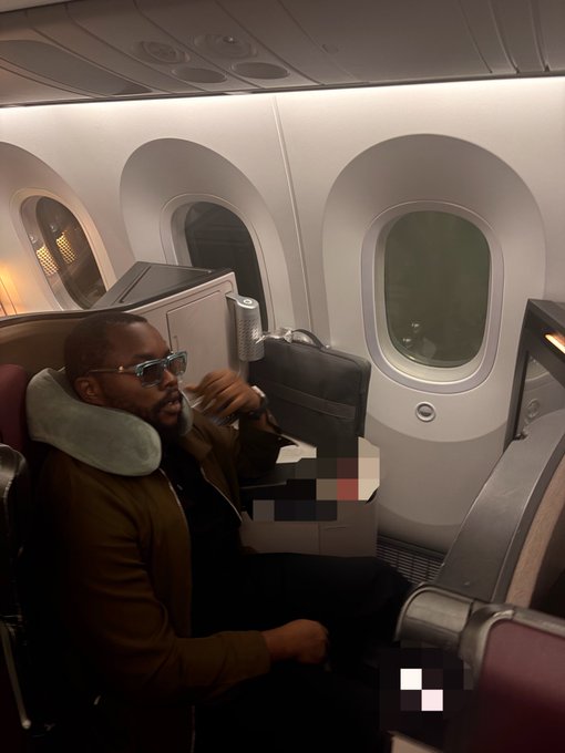 A man wearing sunglasses and a neck pillow relaxes in a premium airline cabin, with a briefcase resting on his lap. The luxurious travel setting complements the post's celebratory tone, reflecting the rewards of success in the web3 space.
