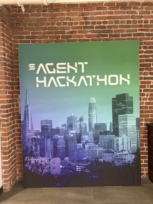 A banner displayed against a brick wall reading 'AGENT HACKATHON' above a purple-tinted cityscape image.