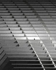 Black and white photograph looking up at a modern building facade with angular, protruding architectural elements.