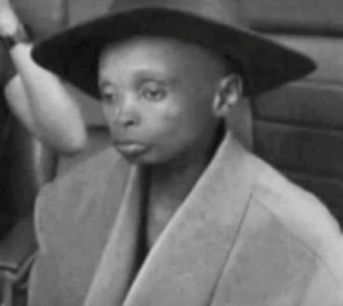 A black and white photo of a young boy wearing a wide-brimmed black hat and an oversized light-colored jacket, looking off to the side.