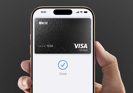 A hand holds a smartphone displaying an OKX Visa Platinum virtual card on the screen, with a blue checkmark and "Done" confirming a successful transaction. The image visually reinforces the post's message about the OKX virtual card's operational functionality within the crypto payments ecosystem.