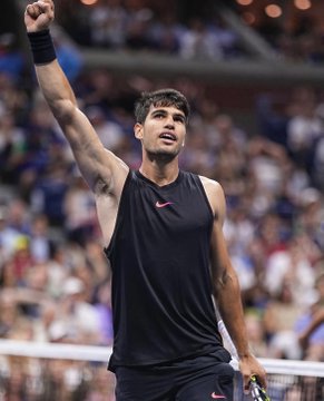 A triumphant Carlos Alcaraz raises his fist in celebration while wearing a black Nike tank top, with a blurred crowd visible behind him at the US Open. The image corresponds to the post highlighting Alcaraz as a top-backed favorite, with betting odds of 80¢ yielding $25,029 for the "chalky" $2.3M tennis wallet.