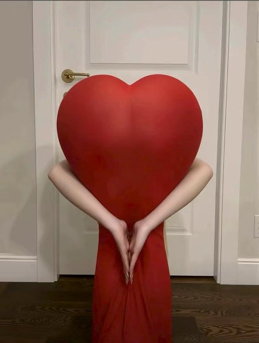 A person conceals their identity behind a large red heart costume while standing in front of a white door, their hands clasped behind the heart. The image symbolizes love and hope for the crypto market, aligning with the post's optimistic sentiment about the bull market and the anticipation of TGEs (Token Generation Events) for projects like @quipnetwork.