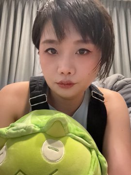 A selfie of a young woman with short dark hair holding a green plush toy shaped like a character from a popular animated film.