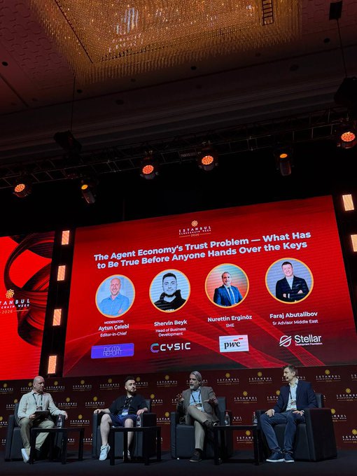 The image shows a group of five people sitting around a table, likely at an event or conference. They are engaged in conversation with each other, possibly discussing a topic related to trust in an increasingly agentic world. The backdrop features a large screen displaying the names of four panelists and their organizations, which include PwC, CcycIC, Starlar, and others.