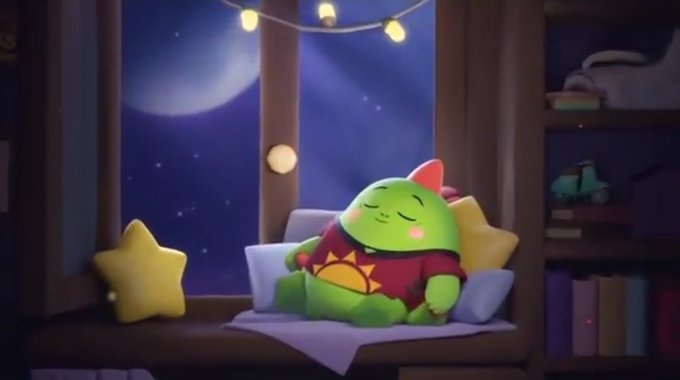 The image features a cartoon green monster sitting on top of a bed next to a window at night. The monster appears to be sleeping or taking a nap while wearing a red shirt with a sun design. There are also two stars placed near the monster, adding to the overall scene. The background shows a bookshelf filled with various items and a clock hanging above it.