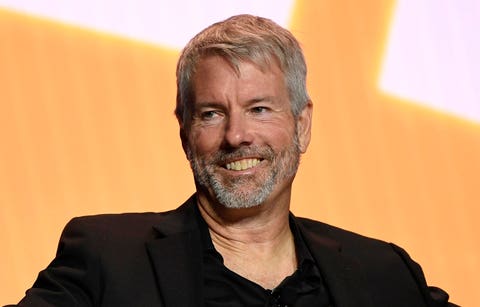 "The man sits in a chair smiling at the camera".