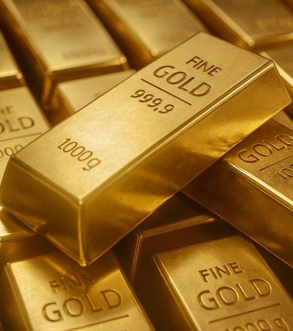 A close-up photograph of stacked gold bars stamped 'FINE GOLD 999.9 1000g', gleaming under warm lighting.