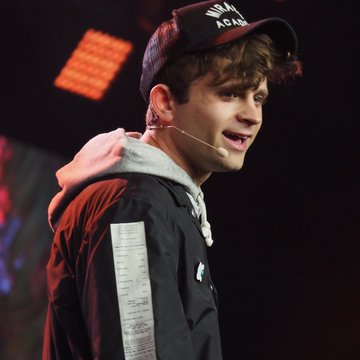 A young man speaks on stage wearing a black cap that reads "NAPALM ACADEMY" and a black jacket over a gray hoodie, with a headset microphone visible near his cheek. The image accompanies a quote from Jack Mallers promoting Bitcoin as a tool for monetary freedom, suggesting the speaker is delivering this pro-Bitcoin message at a live event.