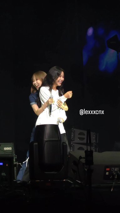 The image shows two smiling women sharing a warm hug on stage, holding microphones mid-performance. The watermark "@lexxxcpx" appears in the text, and the post caption "my moonsun" suggests this is a fan's affectionate reference to the duo's bond.