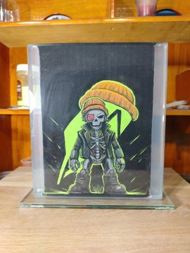 A small painting inside a glass display case showing a skeletal alien-like figure wearing a large sombrero, surrounded by a neon green glow.