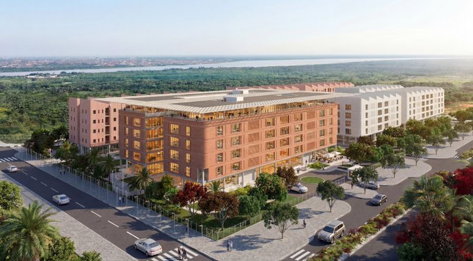 An architectural rendering of a large multi-story pink and white commercial complex with landscaped grounds, palm trees, and surrounding roads.