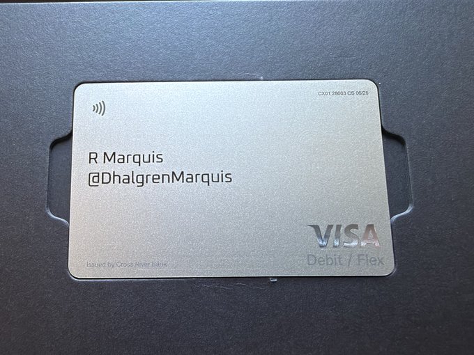A sleek metal Visa Debit/Flex card issued by Cross River Bank displays the name "R Marquis" and username "@DhalgrenMarquis" with a contactless payment symbol. The image illustrates the customizable display feature referenced in the post, showing how users can choose whether their full name appears on the card.