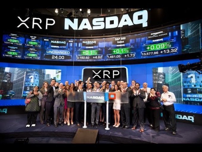 A photograph of the XRP NASDAQ event showing a group of people gathered on stage in front of large screens displaying 'XRP' and various NASDAQ market index data including the S&P 500 and Industrial Average.