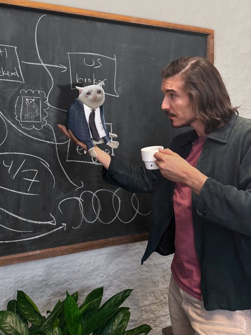 A man holds a coffee cup while pointing at a chalkboard covered in diagrams and arrows, where a small cat in a suit and tie sits beside a box labeled "US broker." The scene humorously ties to the post about Robinhood's DRIP (Dividend Reinvestment Plan), depicting a casual brainstorming session for the brokerage feature.