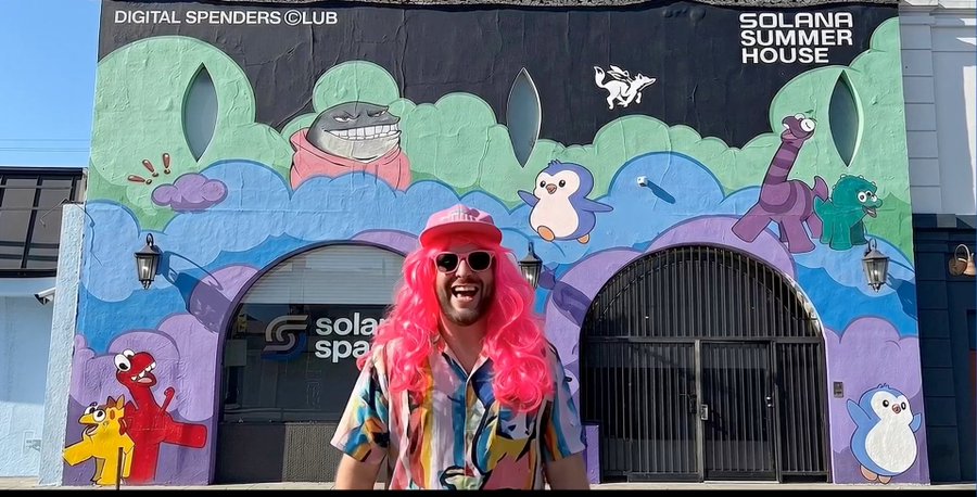 A man wearing a pink wig and sunglasses standing in front of a colorful Solana-themed mural labeled 'DIGITAL SPENDERS CLUB' and 'SOLANA SUMMER HOUSE'.