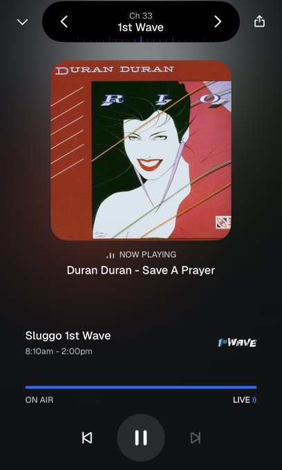 A screenshot of a music streaming app showing "Duran Duran - Save A Prayer" now playing on Sluggo 1st Wave radio station, with on-air times listed as 8:10am - 2:00pm and playback controls at the bottom.