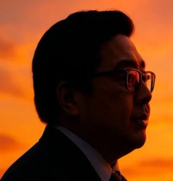 A silhouetted man wearing glasses and a suit is shown in profile against a vivid orange sunset sky, evoking the warm glow that matches the post's caption "Yas."