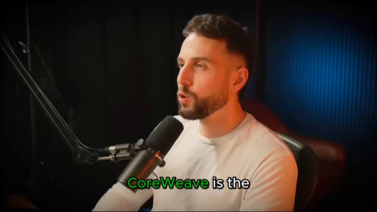 The image features a man sitting at a desk with a microphone attached to his ear. The background of the image is black, which contrasts with the white shirt he's wearing. There are also some words written in green text that read "CoreWeave is the".