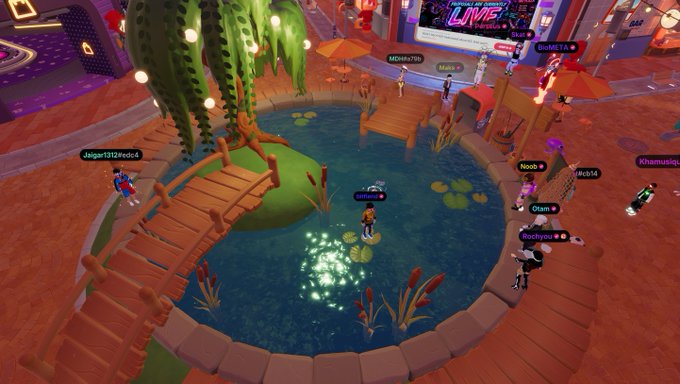 A screenshot of a vibrant virtual world or metaverse game featuring avatars exploring a wooden bridge over a glowing pond surrounded by cacti and colorful lighting.